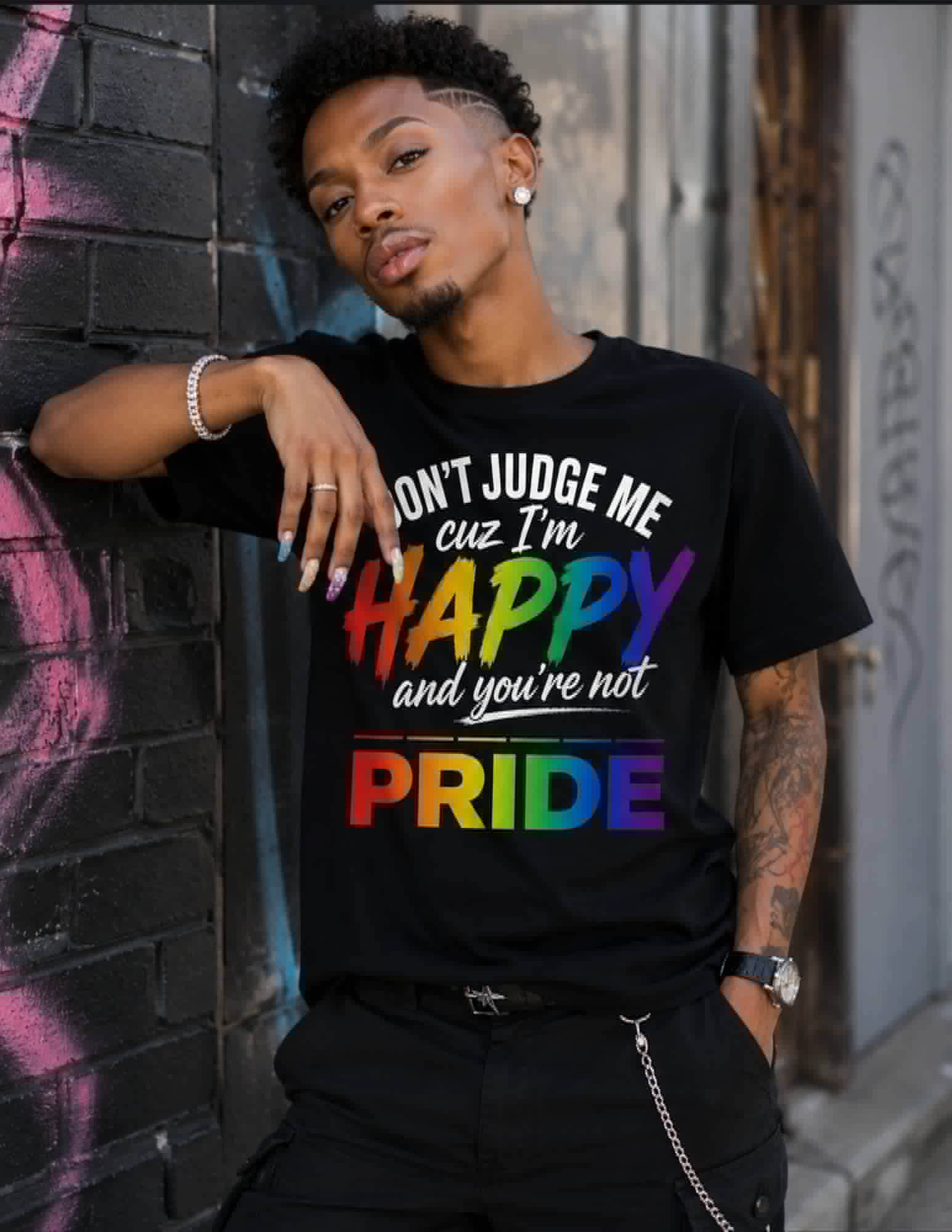 Person wearing a black t-shirt with colorful text leaning against a graffiti-covered wall.